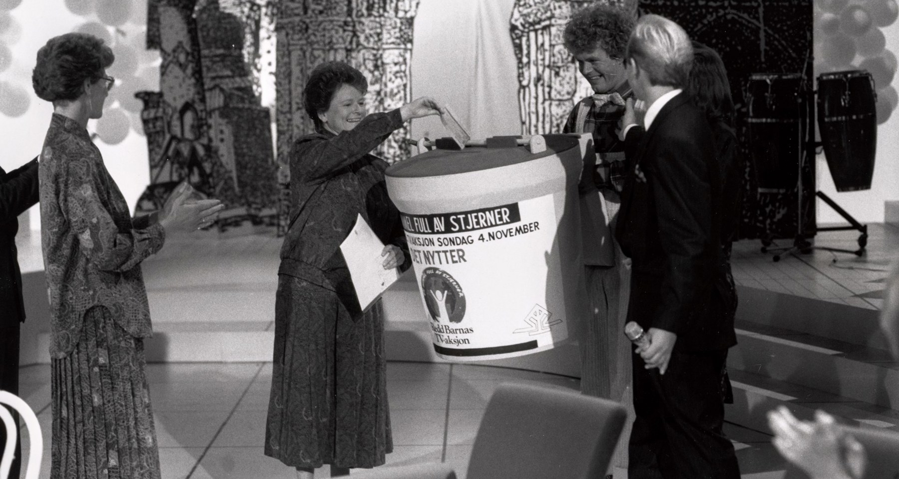 Gro Harlem Brundtland i studio i 1990, gir gave til TV-aksjonen på vegne av regjeringen. Hun putter en sjekk i en stor bøsse, og får applaus av folk rundt.