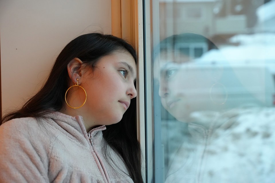 Jente med langt mørkt hår ser lengtende ut av et vindu.