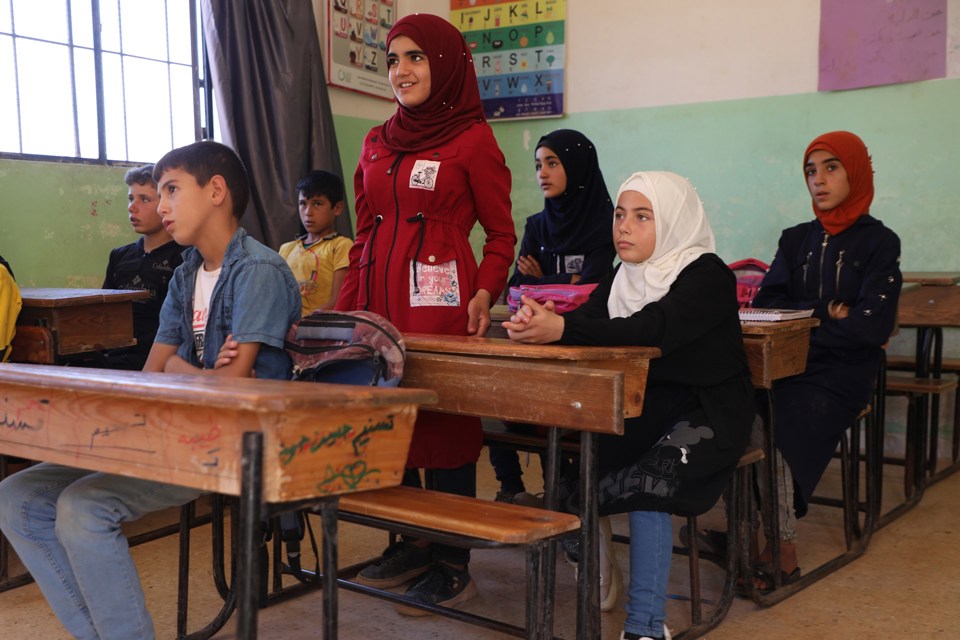 Flere barn som sitter på skolen. Pultene deres er av tre, og har tusjmerker på seg. 