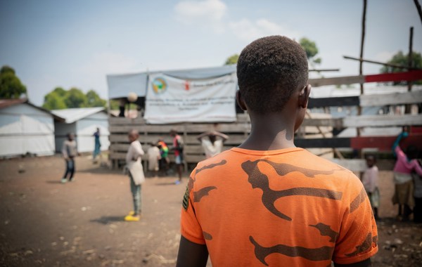 En gutt i oransje tskjorte står med ryggen til kameraet. 