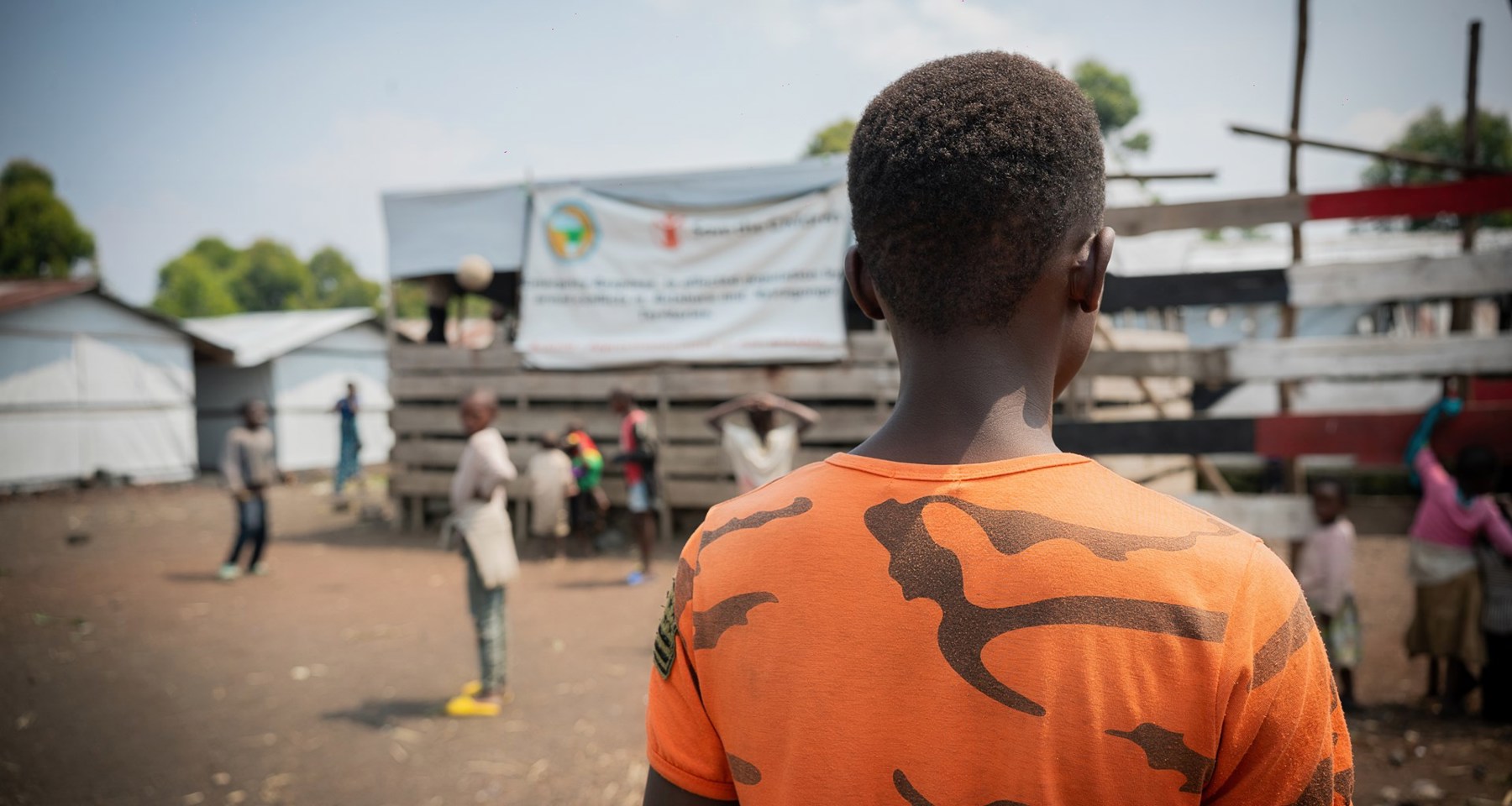 En gutt i oransje tskjorte står med ryggen til kameraet. 