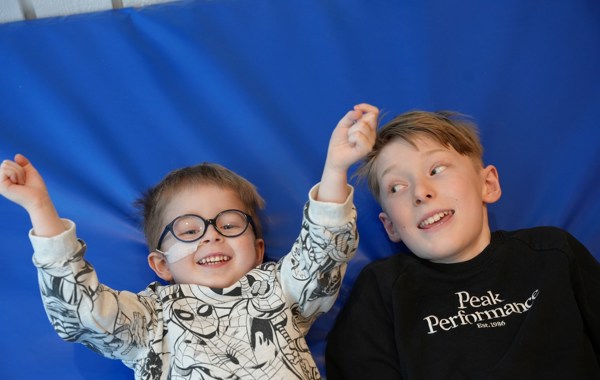 To unge gutter ligger ved siden av hverandre på blått underlag. En av dem har briller og nesesonde.