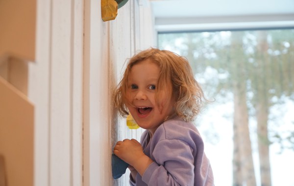 Liten jente lener seg inntil en vegg og smiler