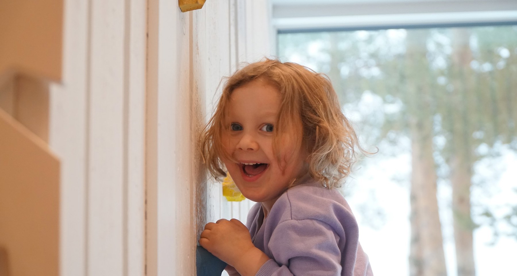 Liten jente lener seg inntil en vegg og smiler